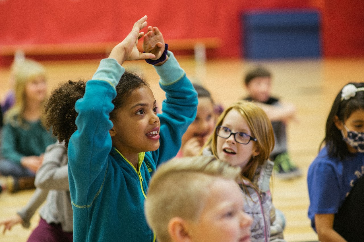 An AEES student gesturing on the gym floor with her classmates.